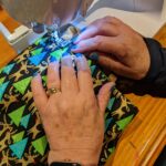 A woman's hands guiding Christmas fabric through a sewing machine